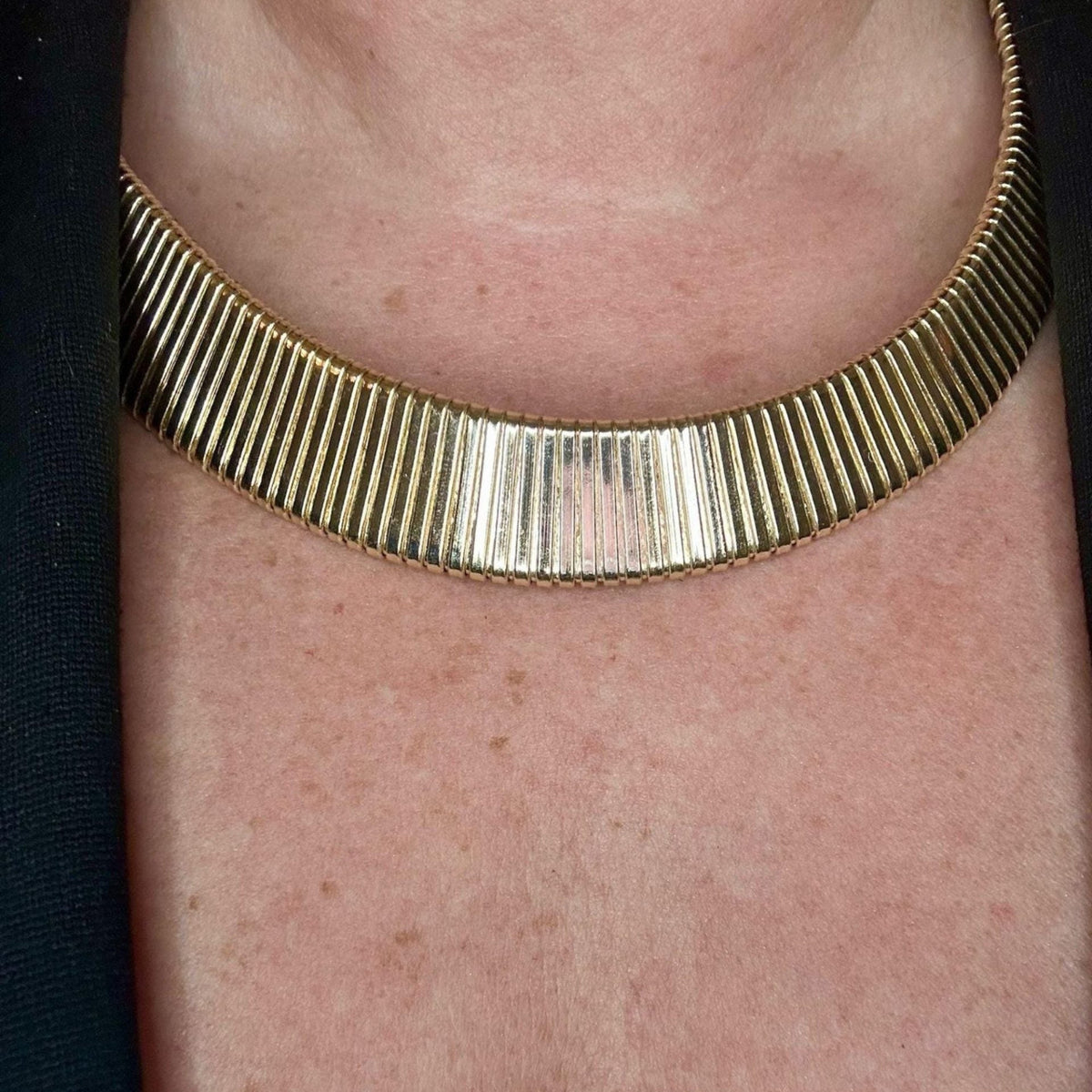Jakris gold-toned ribbed choker necklace worn around the neck, featuring a textured metallic finish.