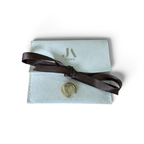 Jakris gold-tone ribbed ear cuff with clear crystals, displayed on a branded light grey pouch with a brown ribbon.