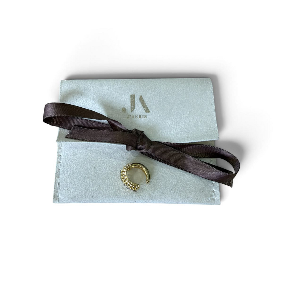 Jakris gold-tone ribbed ear cuff with clear crystals, displayed on a branded light grey pouch with a brown ribbon.