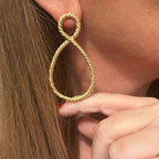 Jakris gold-plated rope-textured hoop earrings with a teardrop infinity design worn on a woman's ear.