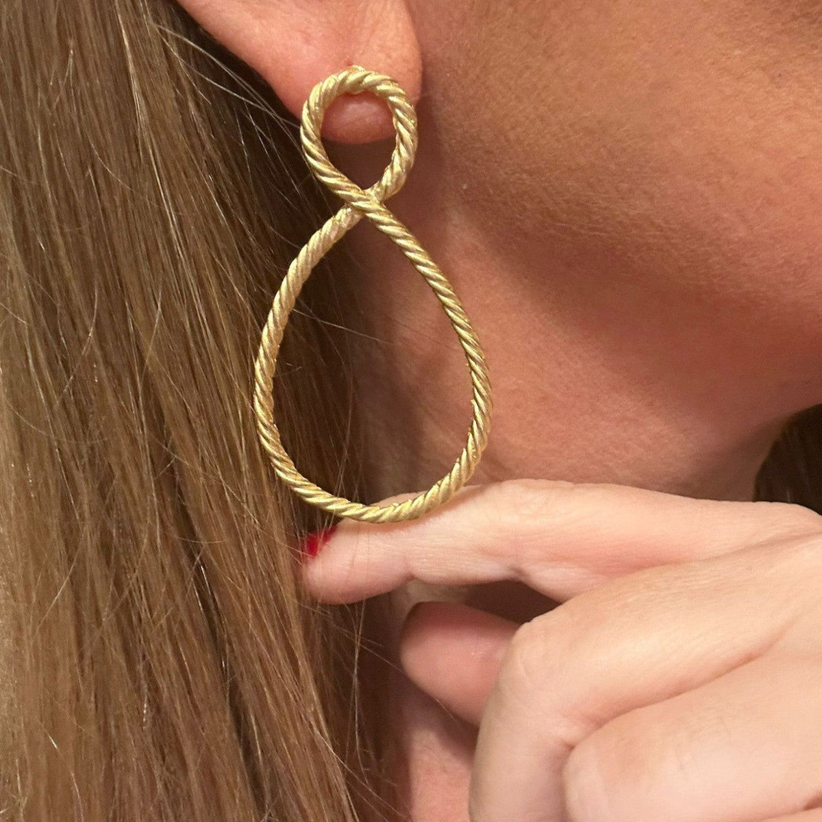 Jakris gold-plated rope-textured hoop earrings with a teardrop infinity design worn on a woman's ear.