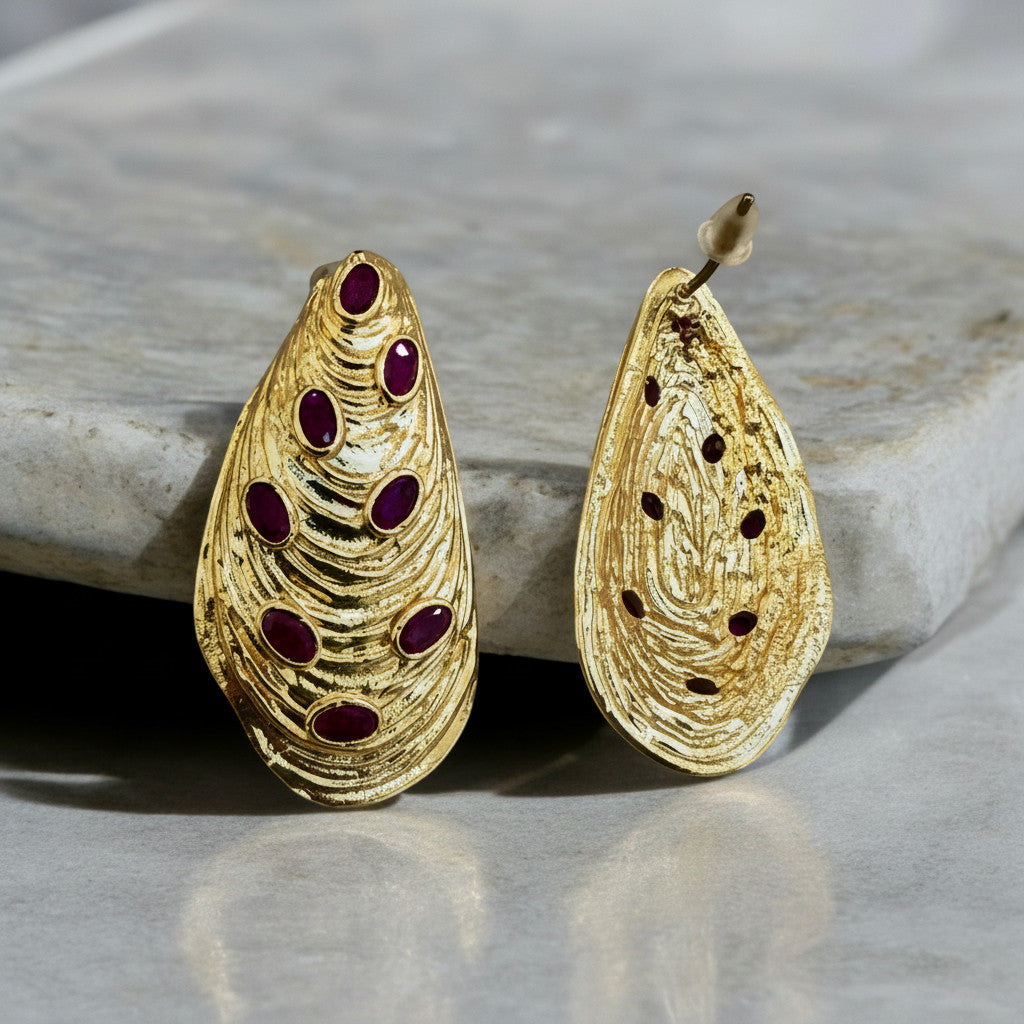 Jakris gold-plated drop earrings featuring textured organic shapes and inlaid oval ruby gemstones on marble surface
