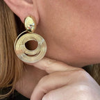 Jakris gold spiral drop earrings with a circular layered design worn on a woman's ear