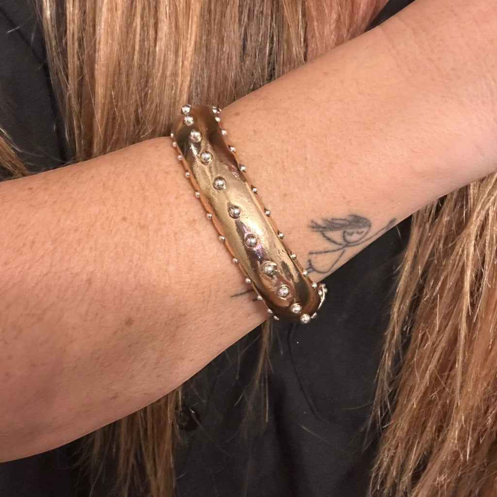 Jakris gold cuff bracelet featuring a polished finish with decorative metal studs worn on a woman's wrist.
