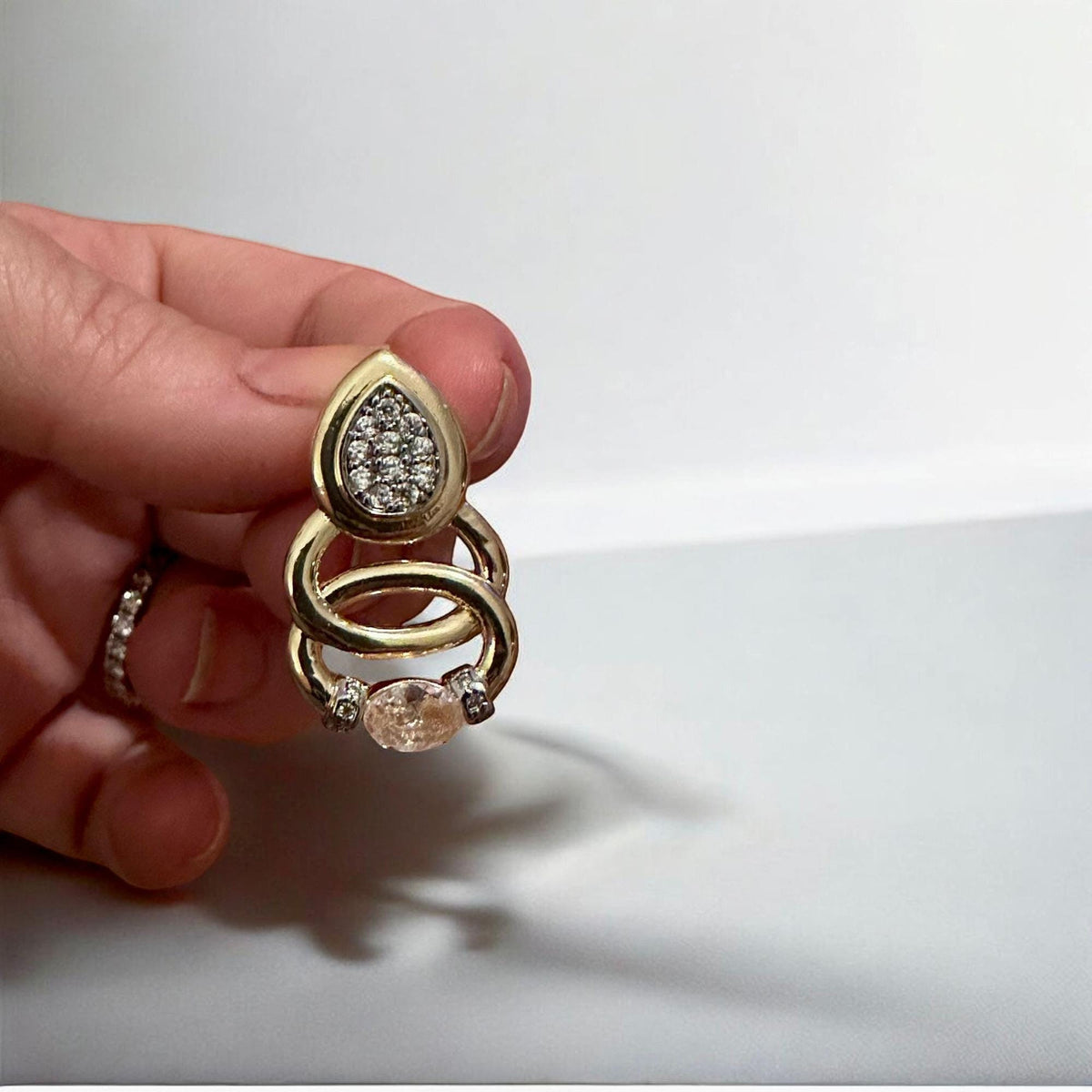 Jakris gold teardrop earrings featuring sparkling pavé stones and circular accents held in a hand