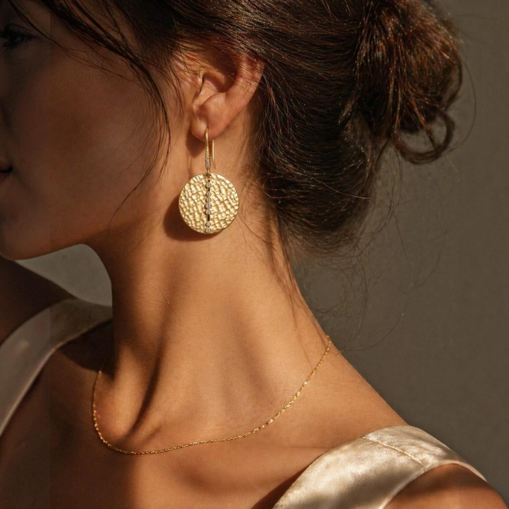 Jakris gold textured disk earrings featuring a vertical line of small sparkling stones worn by a woman