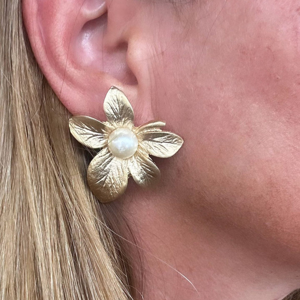 Jakris gold-plated textured flower stud earring with a central pearl detail worn on an earlobe