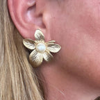 Jakris gold-plated textured flower stud earring with a central pearl detail worn on an earlobe