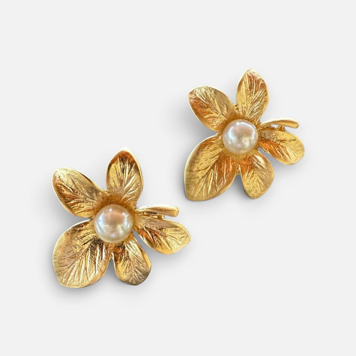 Jakris gold-plated textured flower earrings with a central pearl detail on a neutral surface