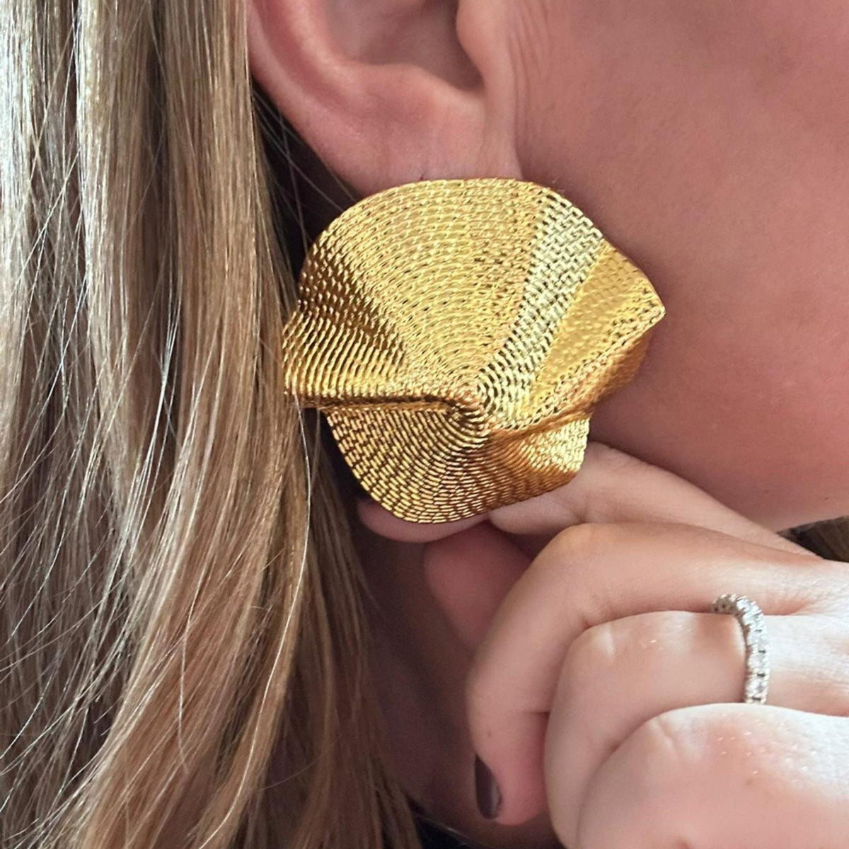 Jakris gold-plated statement earrings featuring a textured folded brass design worn on a model