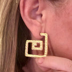 Jakris gold-toned square spiral earrings with a textured artistic finish worn on an earlobe