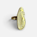 Jakris gold abstract sculptural adjustable ring with a topographic design resting on a white marble surface.