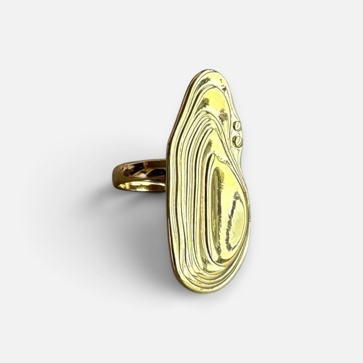 Jakris gold abstract sculptural adjustable ring with a topographic design resting on a white marble surface.