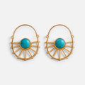 Jakris gold-plated sun-shaped earrings featuring a central turquoise stone, displayed on a beige stone pedestal.