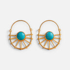 Jakris gold-plated sun-shaped earrings featuring a central turquoise stone, displayed on a beige stone pedestal.