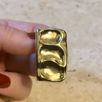 Jakris gold rectangular earring with a wavy, textured surface held between fingers