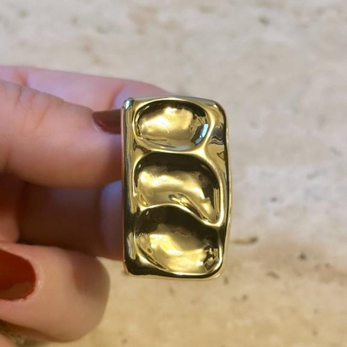 Jakris gold rectangular earring with a wavy, textured surface held between fingers