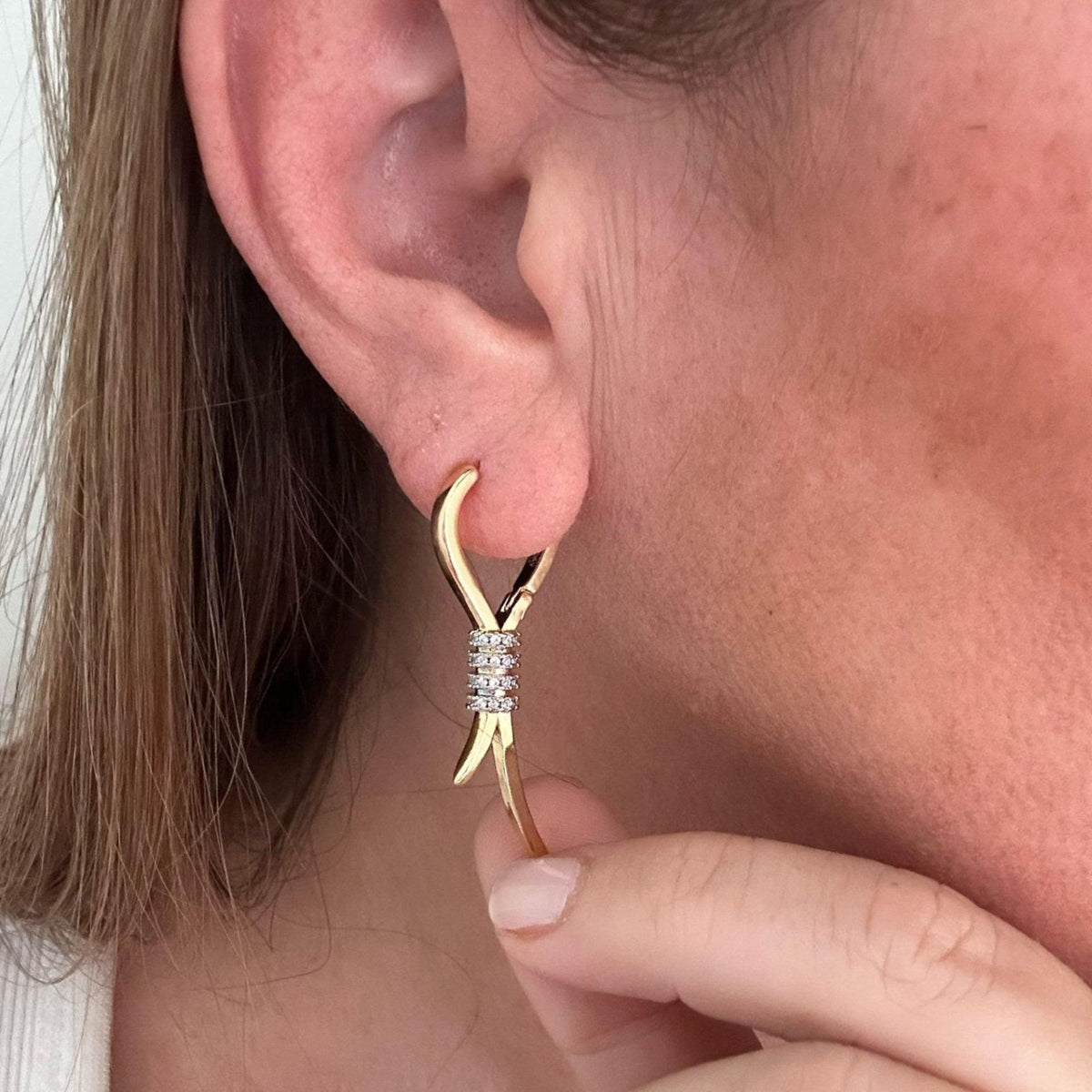 Jakris elegant gold dangling earrings with ribbon-style design and sparkling zircon stone accents on a woman's ear.