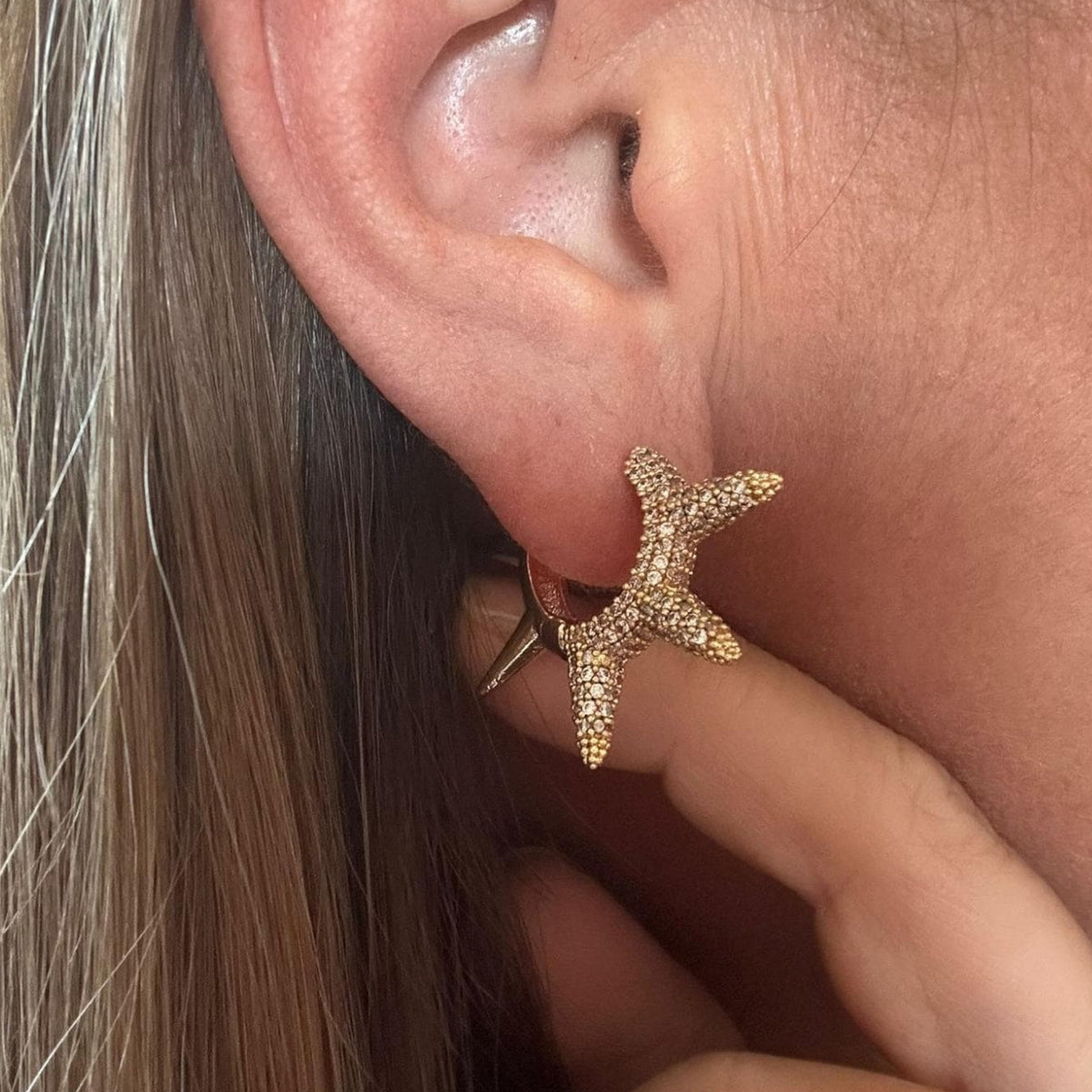 Jakris gold hoop earring with sparkling zircon stones in a sunburst design worn on an earlobe