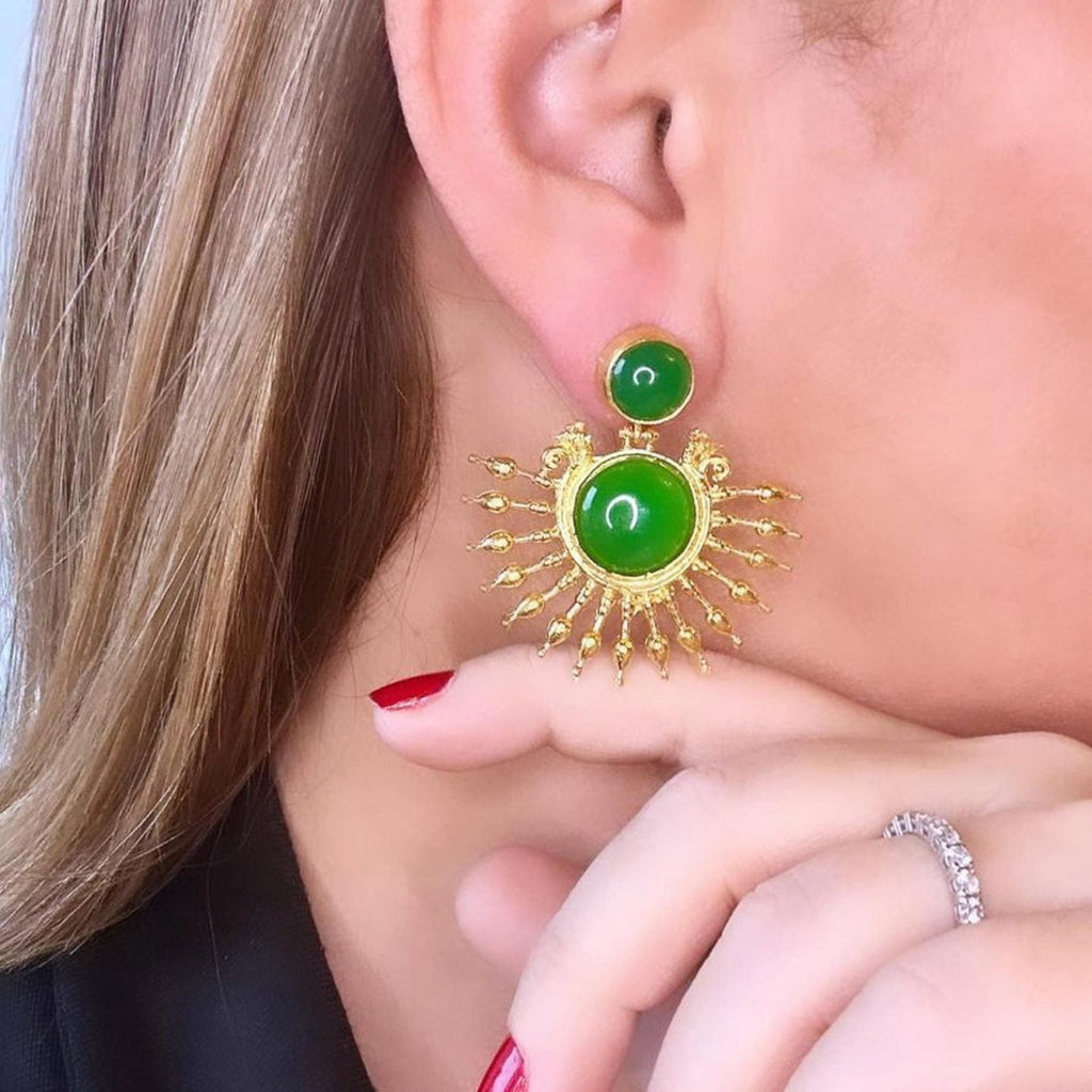 Jakris gold-plated sun-shaped drop earrings featuring green onyx stones worn by a woman with red nail polish