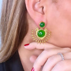Jakris gold-plated sun-shaped drop earrings featuring green onyx stones worn by a woman with red nail polish