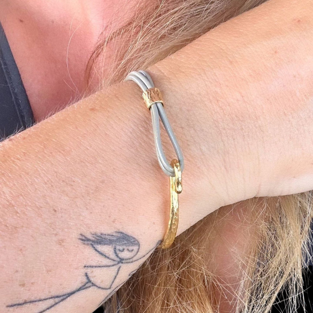 Jakris thin grey leather bracelet with a textured gold-plated bronze cuff detail worn on a wrist.