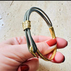 Jakris thin grey leather bracelet with textured gold-plated bronze cuff and hook clasp held in a hand