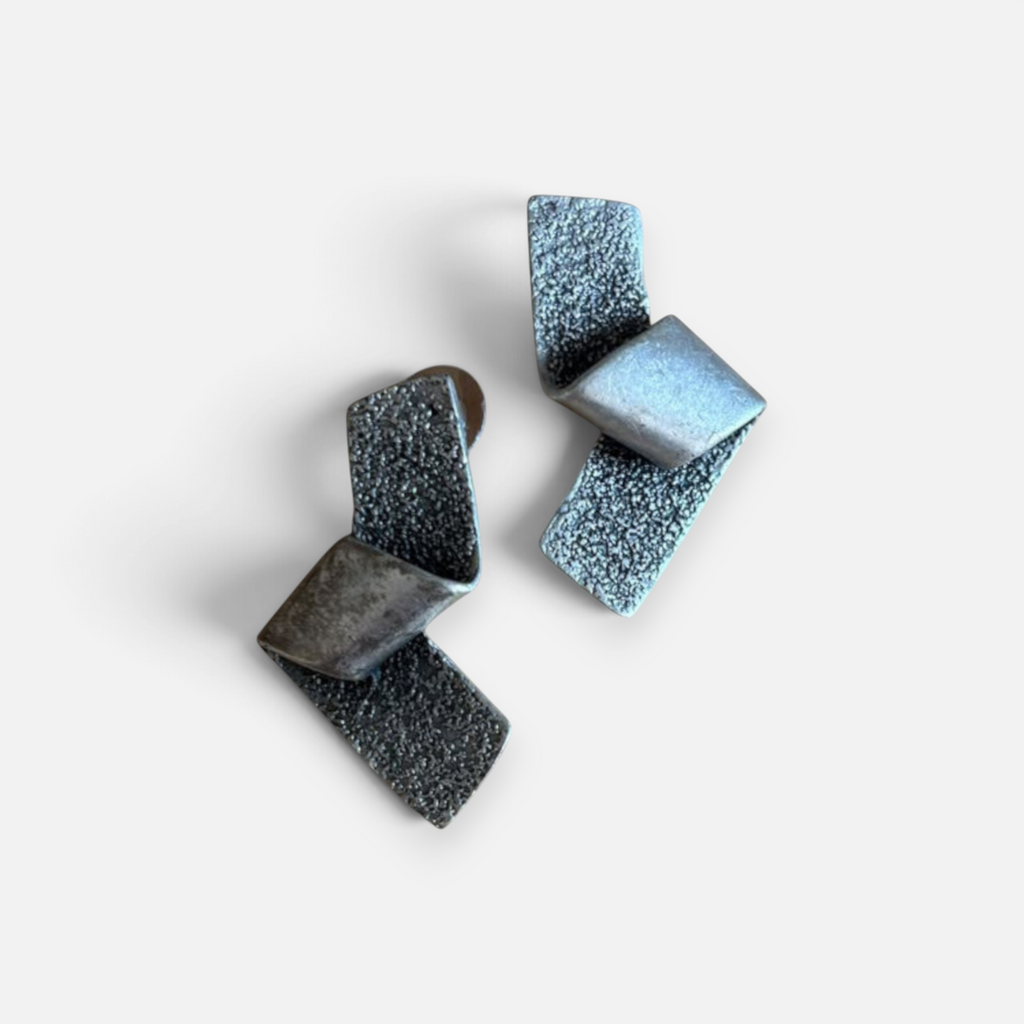 Jakris gümüş renkli, mat ve pürüzlü yüzeyli, modern geometrik tasarımlı şık metal küpe çifti.