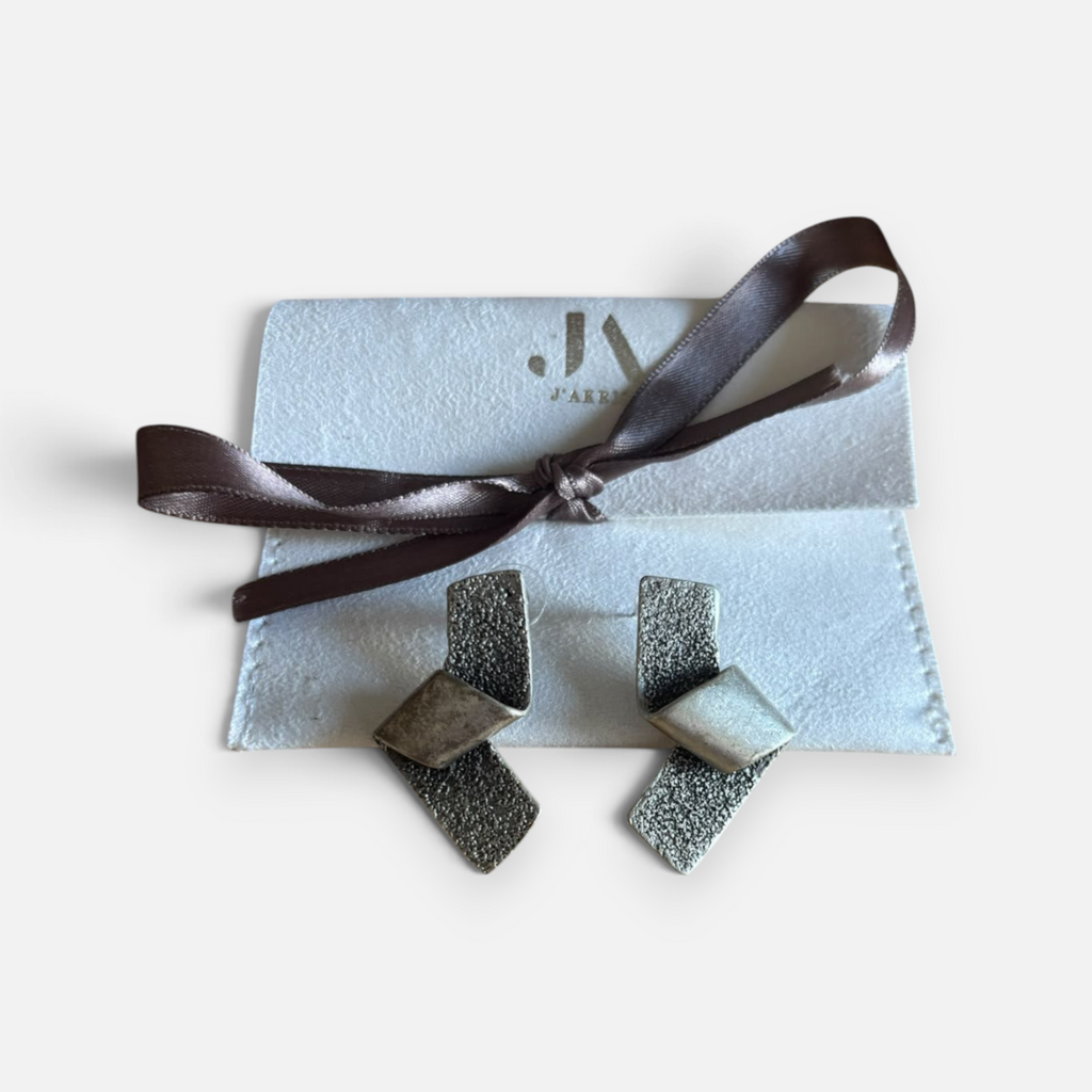Jakris marka, mat ve pürüzlü yüzeyli, gümüş renkli, modern geometrik tasarımlı şık metal küpe çifti.