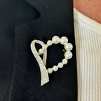 Jakris heart-shaped gold brooch featuring white pearls and sparkling crystals pinned to a black blazer lapel