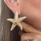 Jakris large starfish enamel earrings in beige and gold worn on a woman's ear for a summer beach style look
