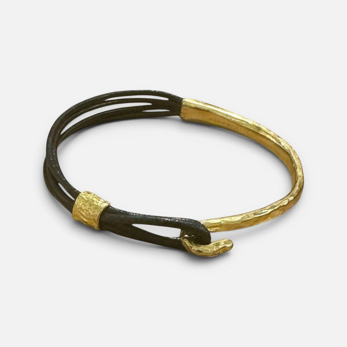 Jakris thin leather bracelet featuring a textured gold-plated bronze cuff and hook closure.