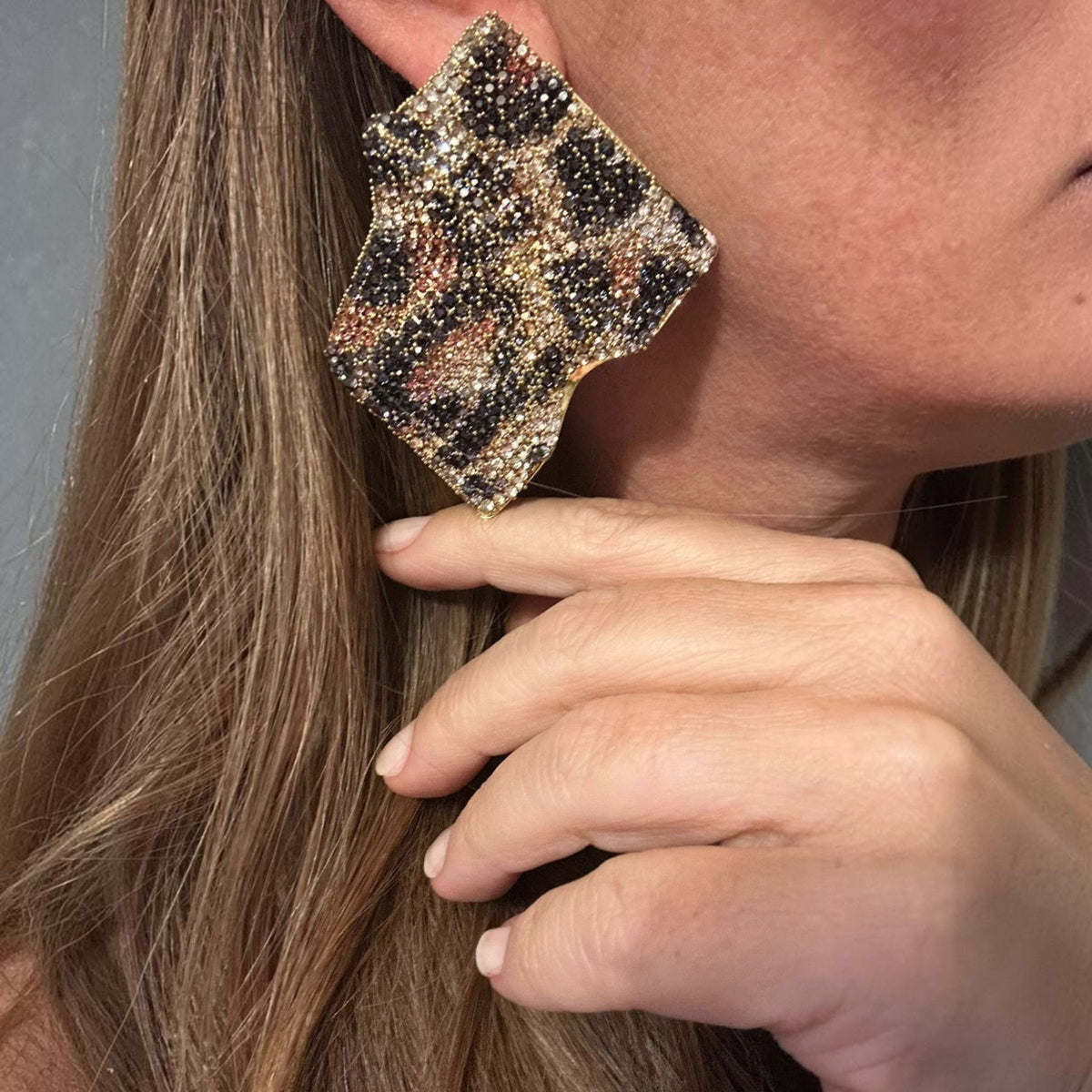 Jakris statement earrings with leopard print crystal stones and gold-plated brass, worn on a woman's ear.