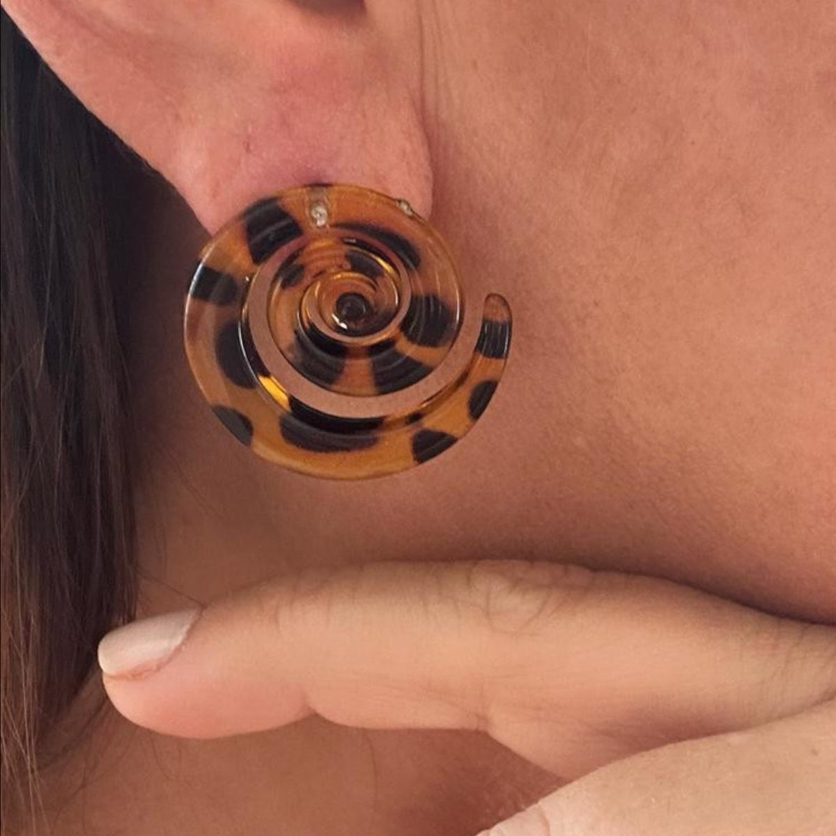 Jakris tortoiseshell spiral earrings with a brown and black leopard print pattern worn on an earlobe.