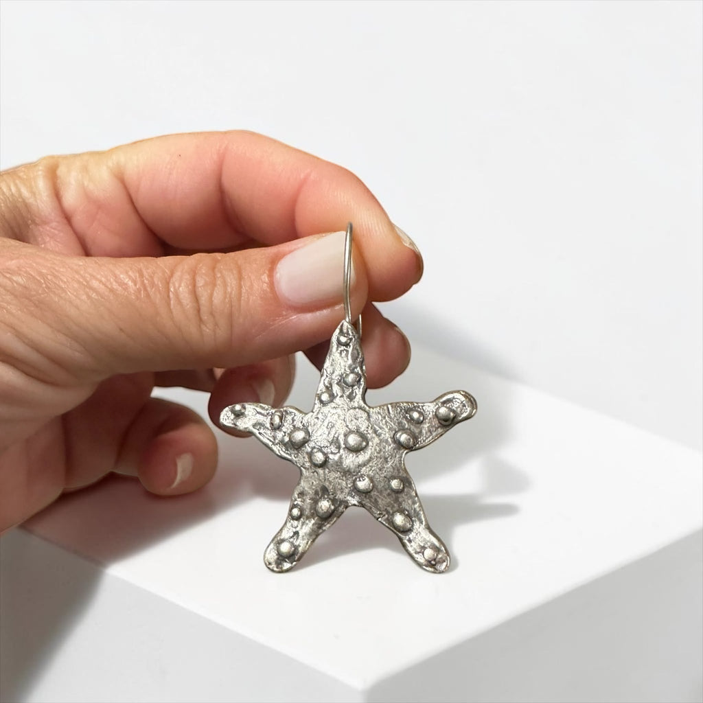 Jakris Maris silver-plated brass starfish earring with a textured surface held by hand against a white background.