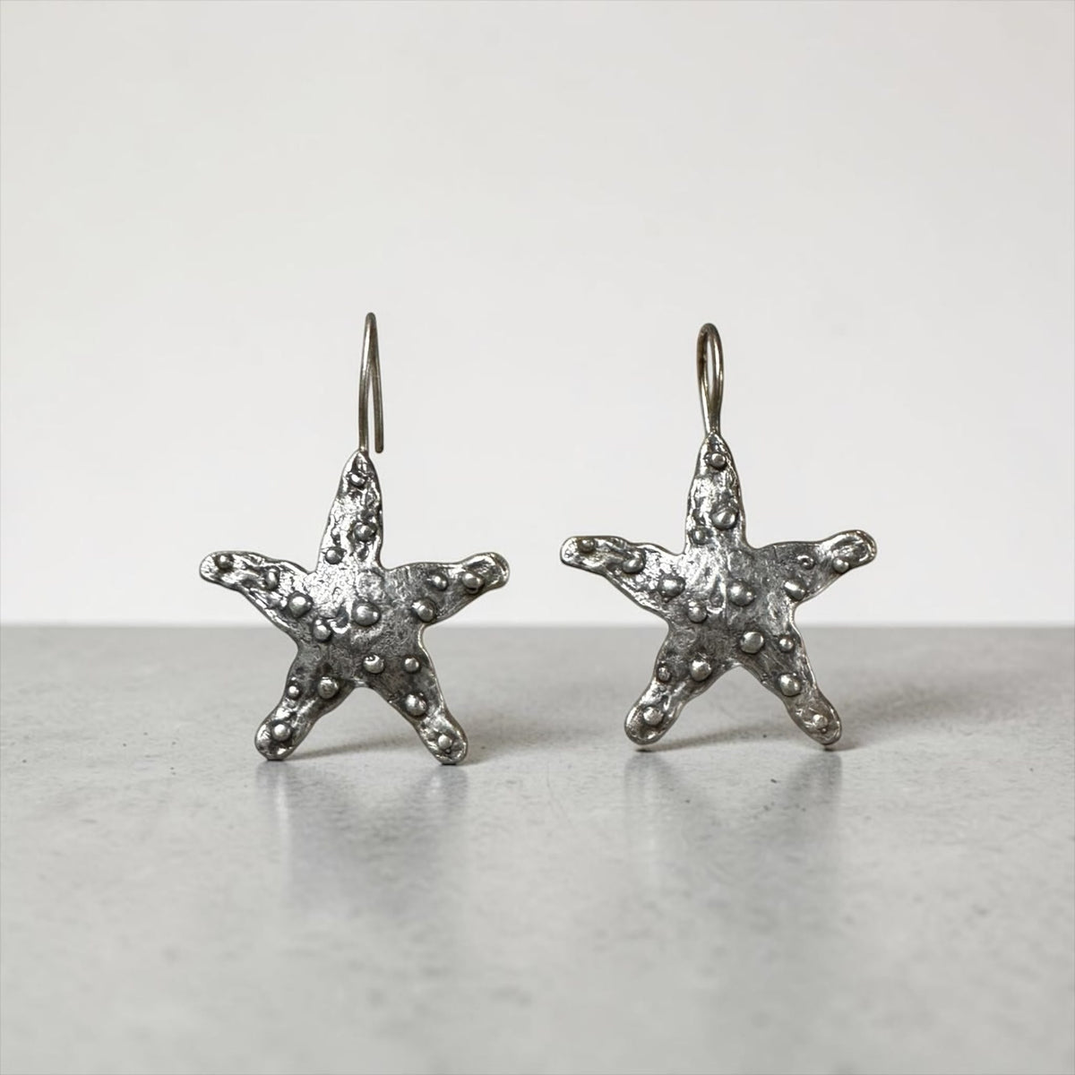 Jakris Maris silver-plated brass starfish earrings with a textured surface and minimalist hook design.