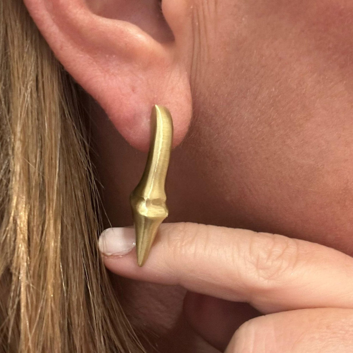 Jakris modern brass earring with a unique pointed, elongated design worn on an earlobe