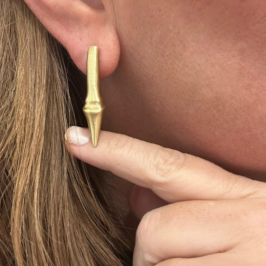Jakris modern brass earring with a unique pointed, elongated drop design worn on an earlobe.