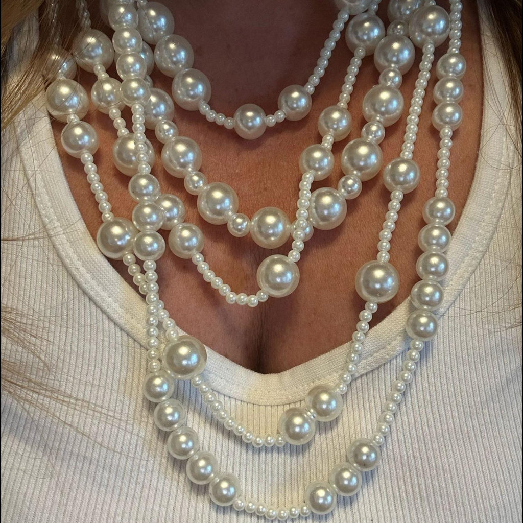Jakris multi-strand long pearl necklace featuring layered white pearls of varying sizes worn over a white top