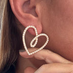 Jakris elegant heart-shaped bridal earrings featuring delicate white pearls worn on a model's ear