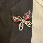 Jakris elegant butterfly brooch featuring pink translucent wings and sparkling crystal accents on a black blazer