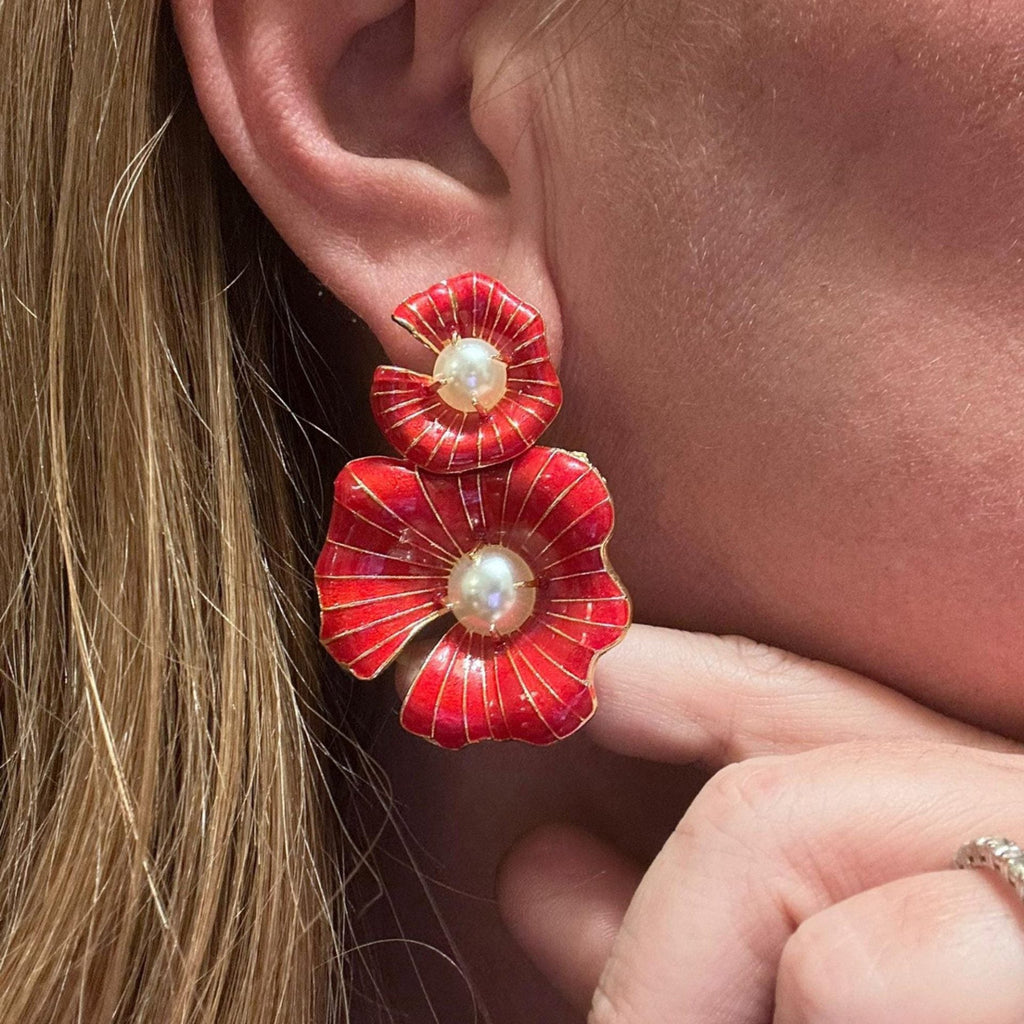 Jakris red enamel flower earrings with central pearl details worn on an ear