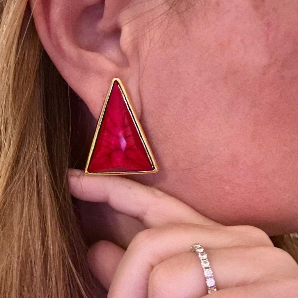 Jakris modern triangle earring with a vibrant red stone and gold-toned frame worn on an earlobe