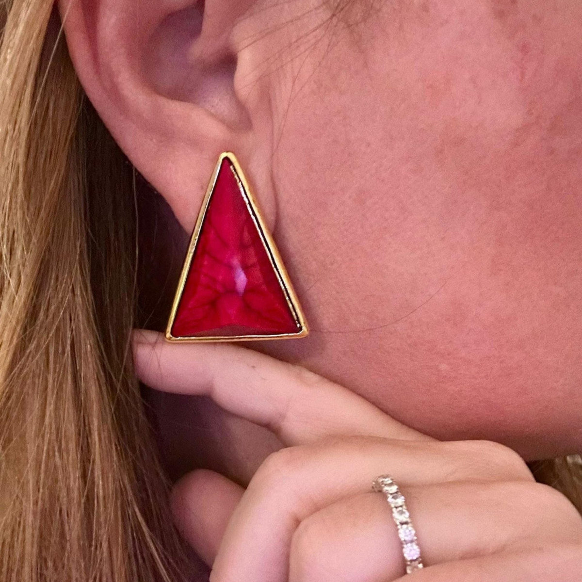 Jakris modern triangle earring with a vibrant red stone and gold-toned frame worn on an earlobe
