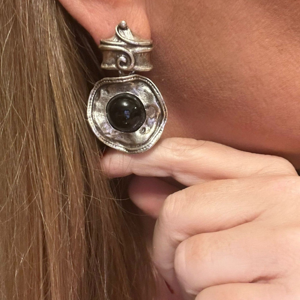 Jakris silver dangle earrings featuring a textured organic metal design and a central black stone worn on an ear