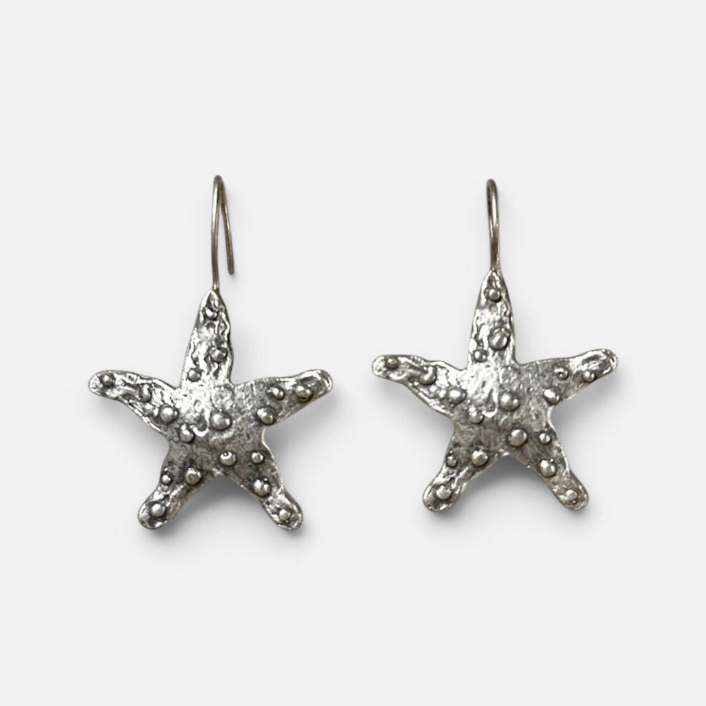 Jakris silver-plated brass starfish earrings with a textured surface on a white fabric background.