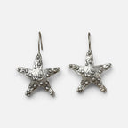 Jakris silver-plated brass starfish earrings with a textured surface on a white fabric background.