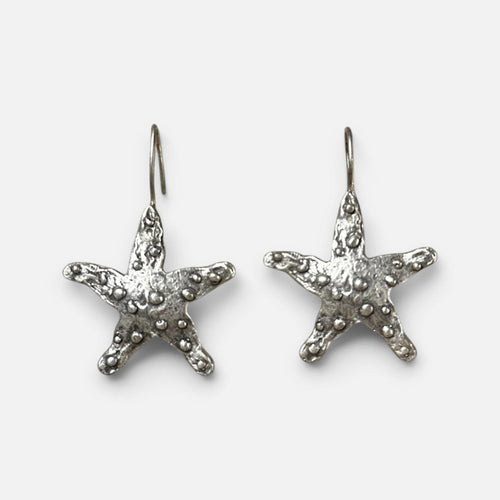 Jakris silver-plated brass starfish earrings with a textured surface on a white fabric background.