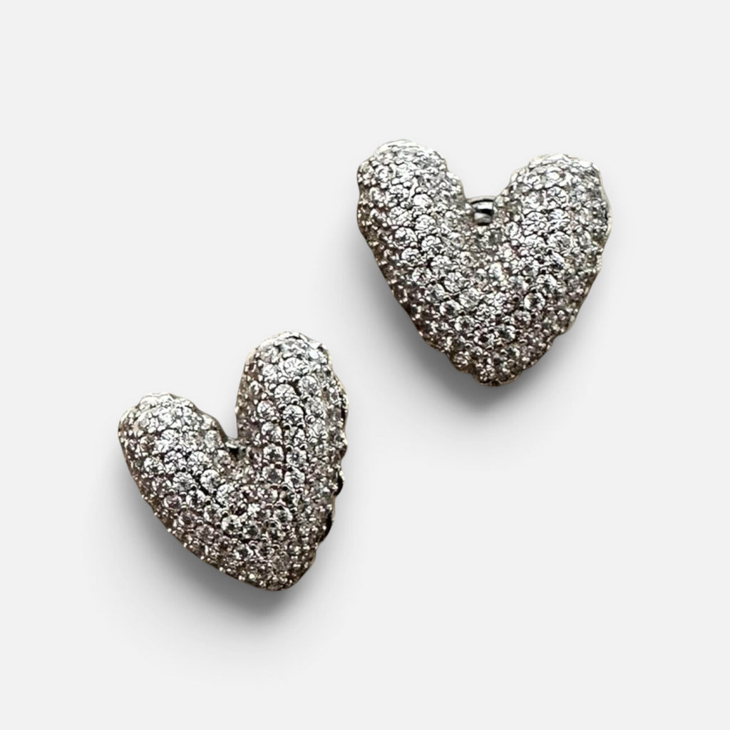 Jakris silver heart-shaped stud earrings covered in sparkling white stones on a white surface