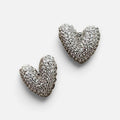 Jakris silver heart-shaped stud earrings covered in sparkling white stones on a white surface